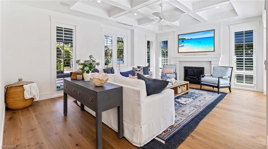Living area featuring coffered ceiling, a glass covered fireplace, light wood-style flooring, recessed lighting, and ceiling fan