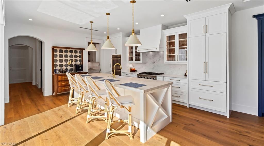Kitchen with a breakfast bar area, arched walkways, pendant lighting, glass fronted cabinets, and an island with sink
