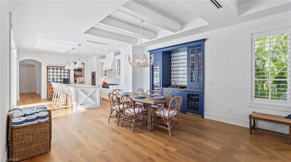 Dining space featuring light wood-style flooring, arched walkways, beverage cooler, hanging lights, and a tray ceiling