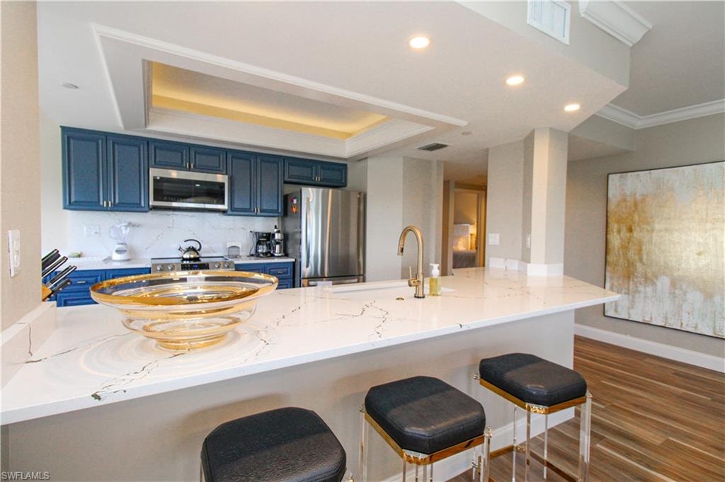 Kitchen with a breakfast bar area, appliances with stainless steel finishes, blue cabinetry, dark hardwood / wood-style floors, and sink