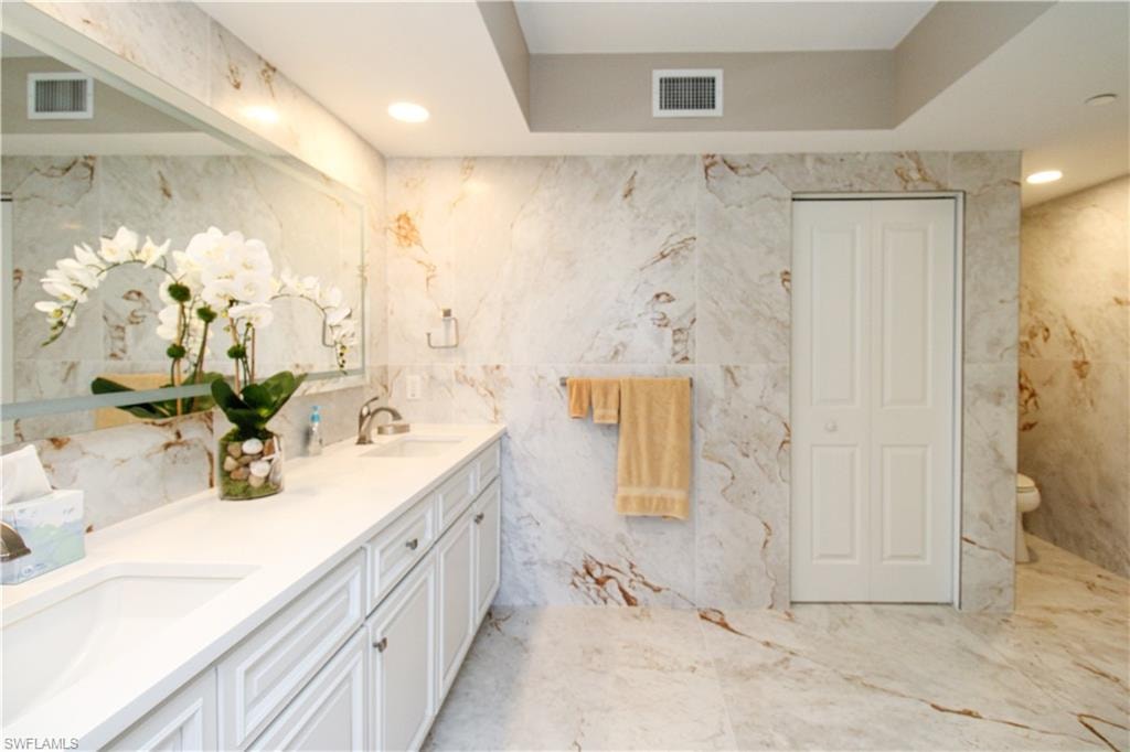 Bathroom featuring tile walls, vanity, a tray ceiling, and toilet