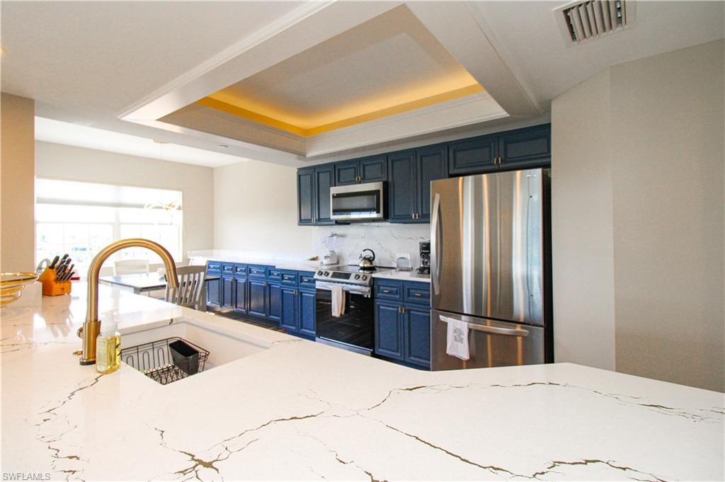 Kitchen with a raised ceiling, appliances with stainless steel finishes, backsplash, blue cabinetry, and sink