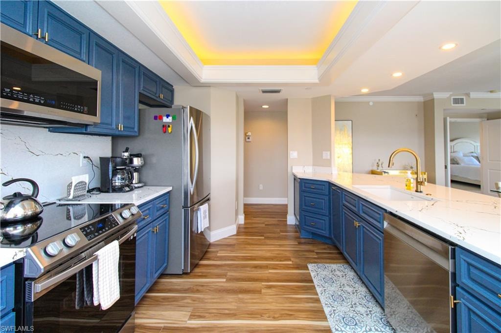 Kitchen with light hardwood / wood-style floors, crown molding, blue cabinets, and stainless steel appliances
