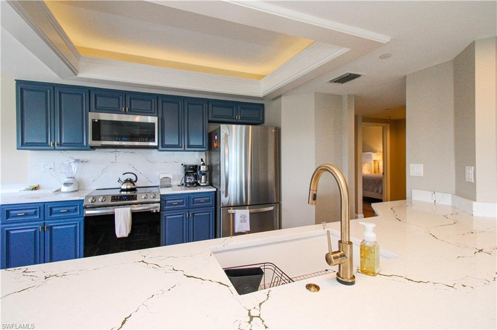 Kitchen with light stone counters, a tray ceiling, blue cabinetry, stainless steel appliances, and sink