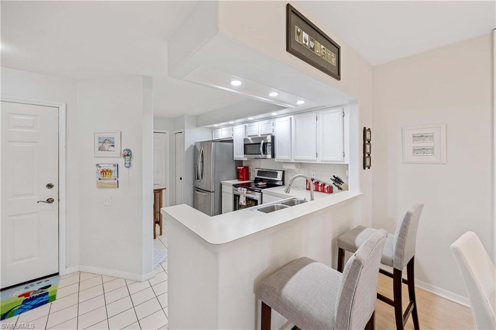 Kitchen featuring stainless steel appliances, a sink, light countertops, baseboards, and a breakfast bar