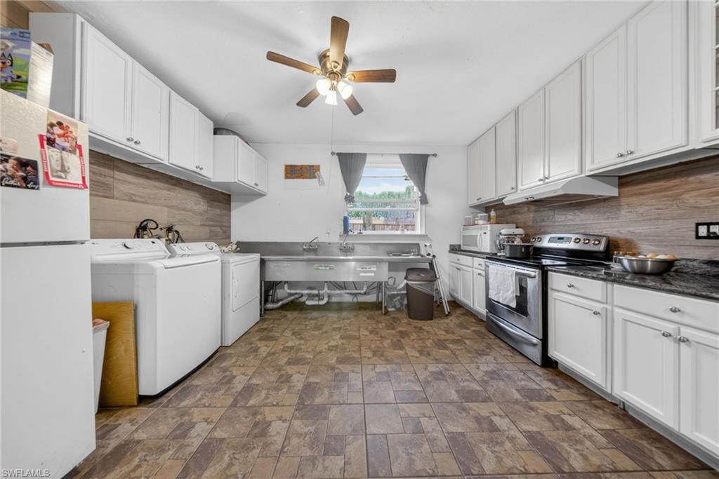 Kitchen with white appliances, white cabinets, ceiling fan, stone finish flooring, and washing machine and clothes dryer