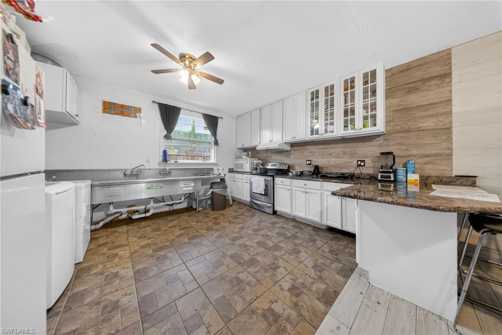 Kitchen featuring white cabinetry, white appliances, glass fronted cabinets, a peninsula, and a kitchen bar