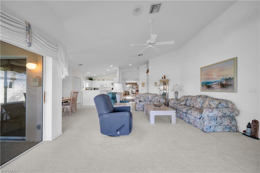 Living area featuring light colored carpet, lofted ceiling, and ceiling fan