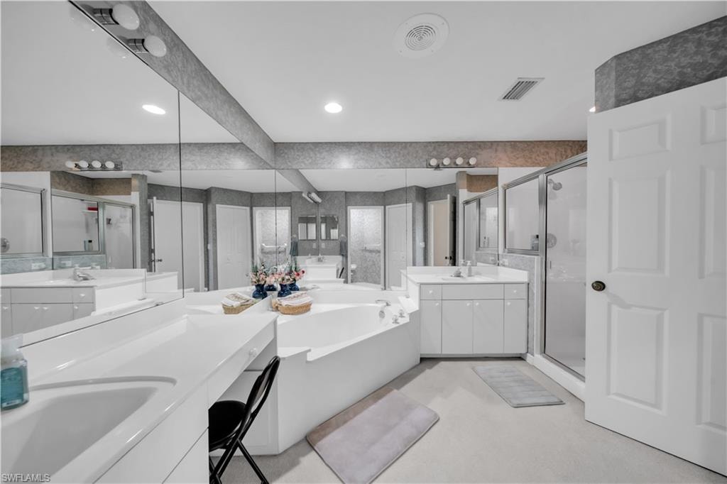 Bathroom featuring two vanities, a bath, a shower stall, and recessed lighting