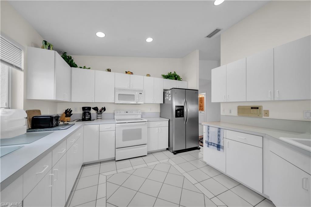 Kitchen featuring white appliances, light countertops, white cabinetry, lofted ceiling, and recessed lighting