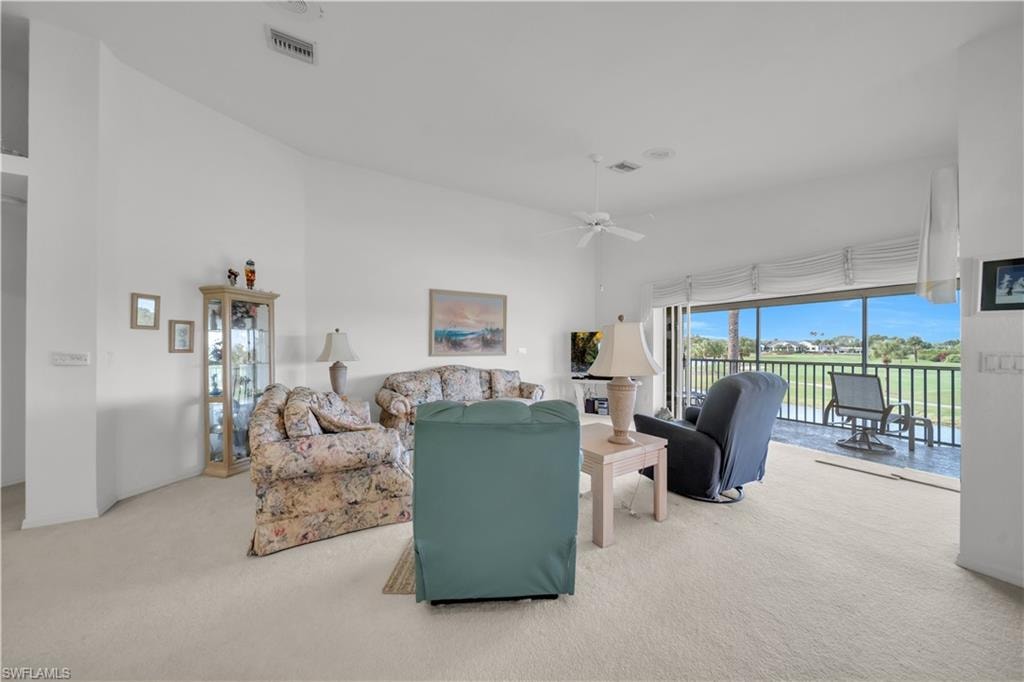 Living room with light colored carpet, a ceiling fan, and a high ceiling