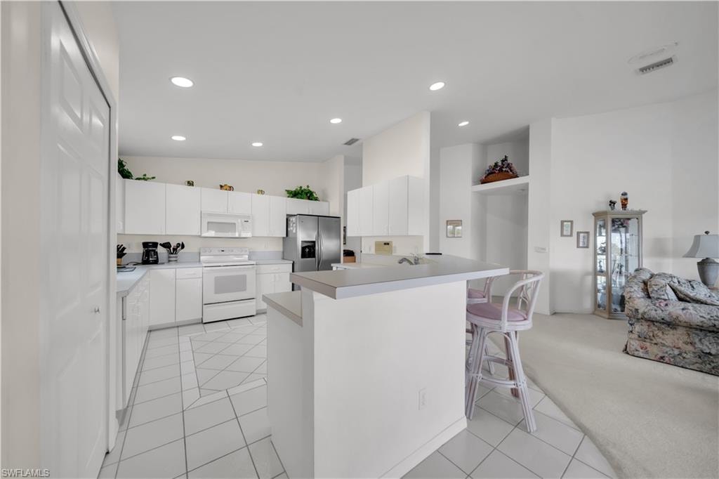 Kitchen with white cabinetry, a breakfast bar, light countertops, white appliances, and recessed lighting