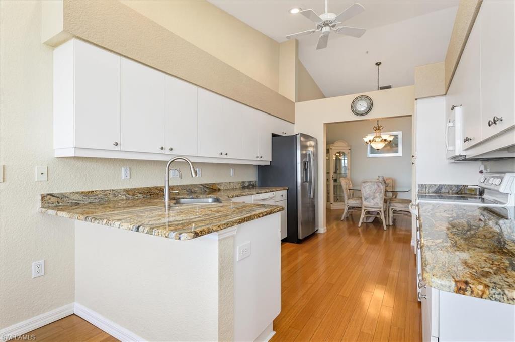 Kitchen with stone counters, white cabinets, a peninsula, wood floors, and ceiling fan