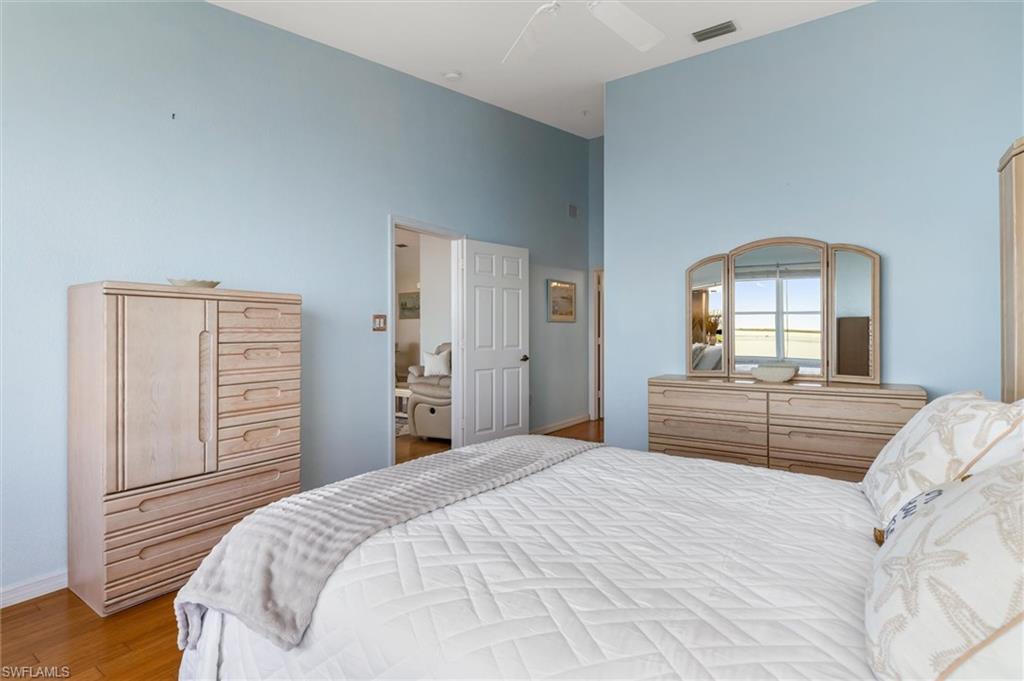 Primary bedroom featuring wood flooring, multiple windows, ceiling fan, vaulted ceiling, walk-in closet and vast water views