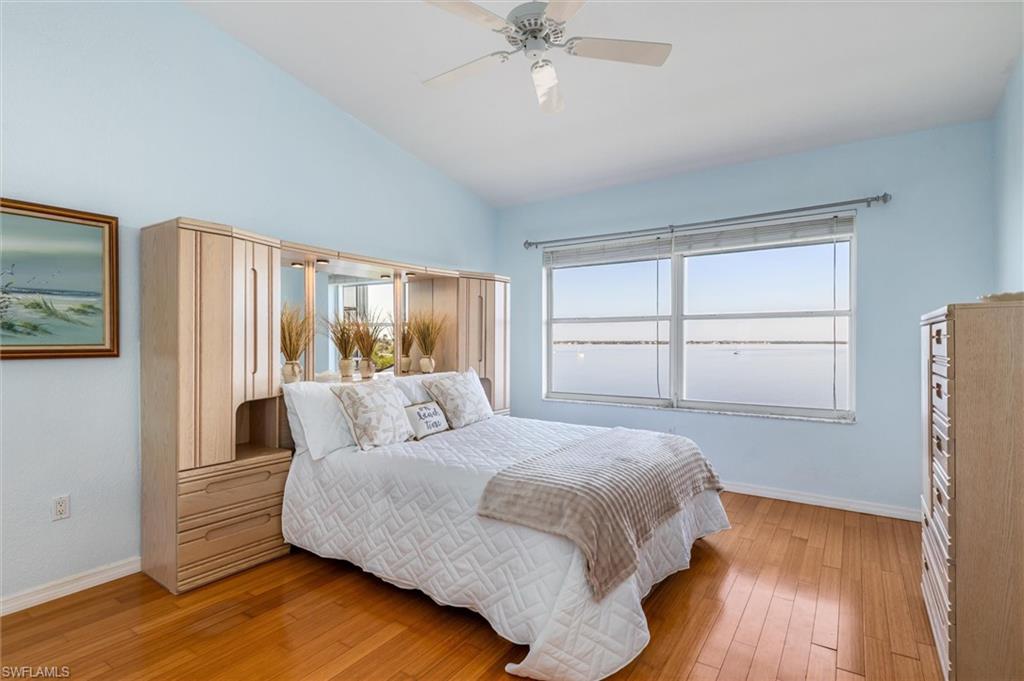 Primary bedroom featuring wood flooring, multiple windows, ceiling fan, vaulted ceiling, walk-in closet and vast water views