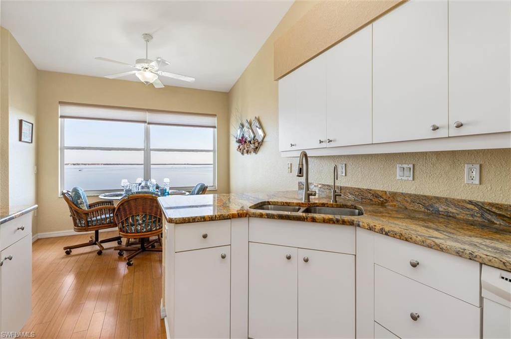 Kitchen with stone counters, white cabinets, a peninsula, wood floors, and ceiling fan