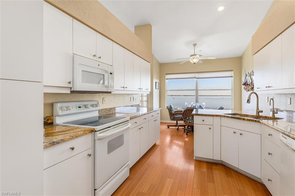 Kitchen with white appliances, white cabinetry, bamboo wood flooring, and ceiling fan