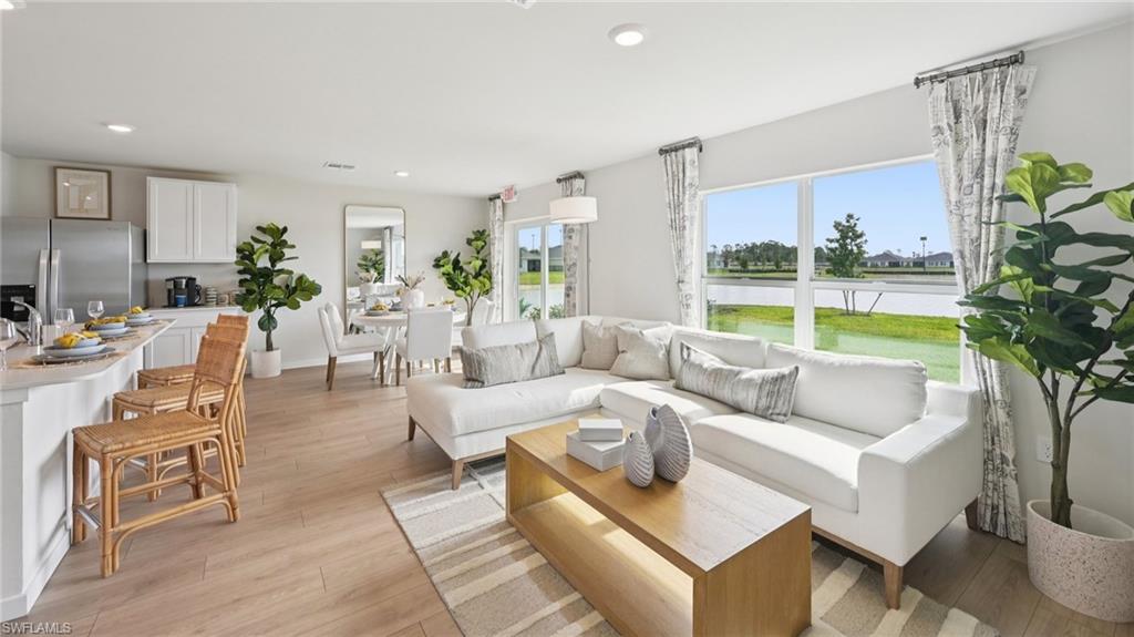 Model Home. This open-concept living area features light wood-look flooring, large windows with views of the surrounding landscape, and a kitchen island with seating
