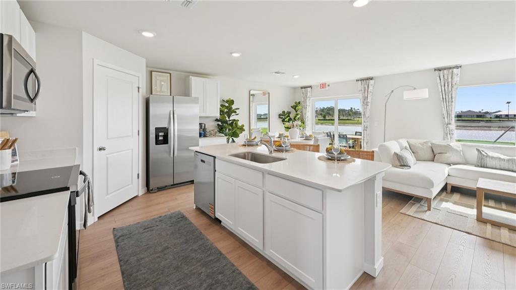Model Home. The open concept living area features light wood flooring, a kitchen island with a sink, white cabinetry, and stainless steel appliances