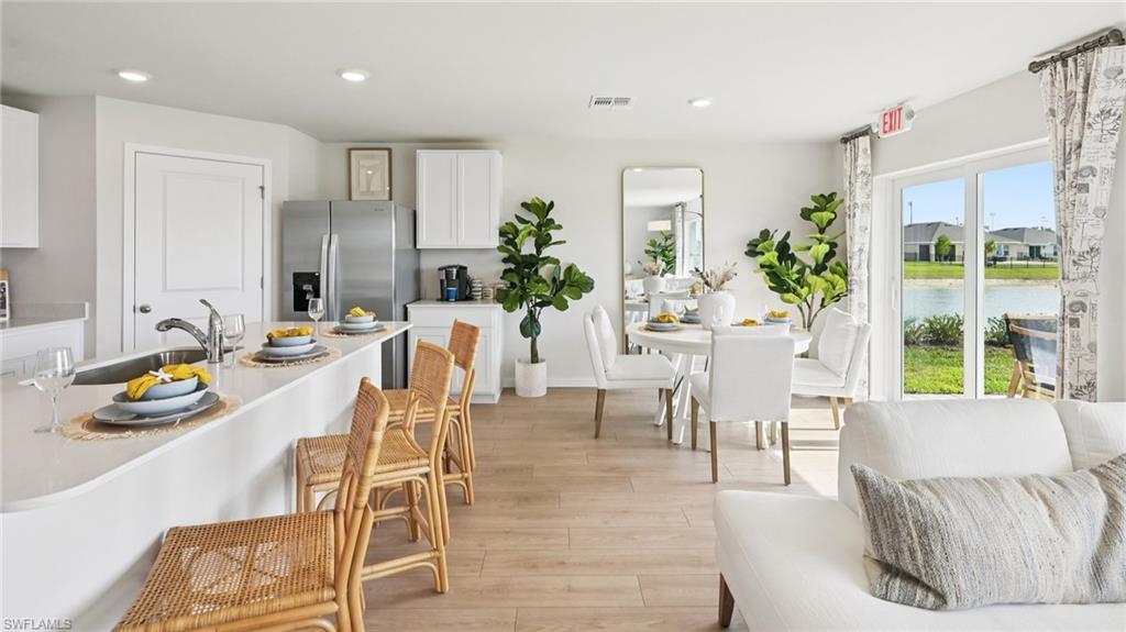 Model Home. Open concept living area featuring light wood-style flooring, a kitchen island with seating, and a dining area with views of the outdoor landscape