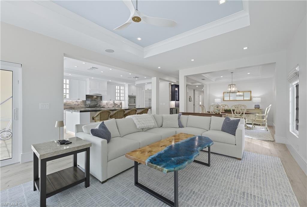 Living room with a tray ceiling, light wood-type flooring, crown molding, ceiling fan, and recessed lighting