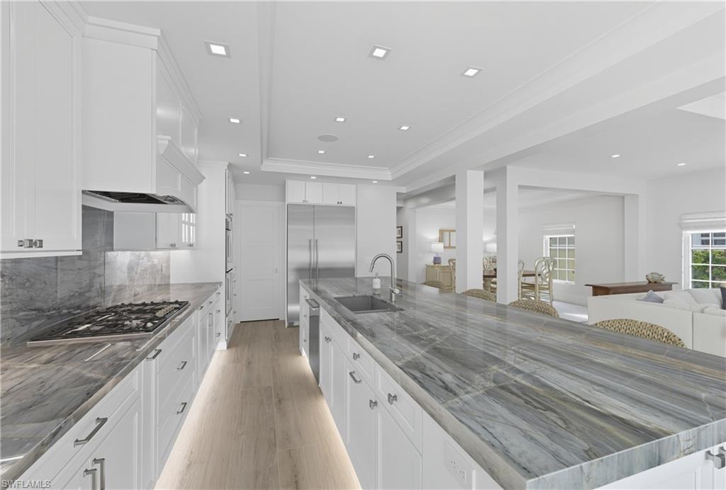 Kitchen featuring white cabinets, light wood finished floors, a spacious island, backsplash, and a breakfast bar