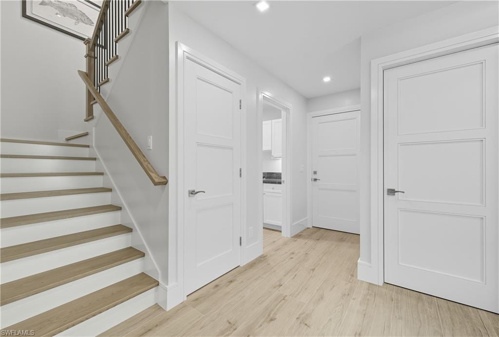 Hallway with stairway, light wood-type flooring, and recessed lighting