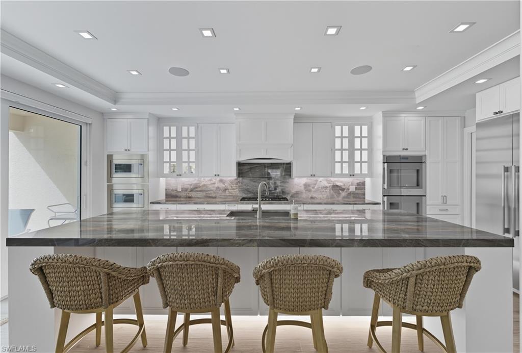 Kitchen with a breakfast bar area, a large island with sink, backsplash, white cabinets, and ornamental molding