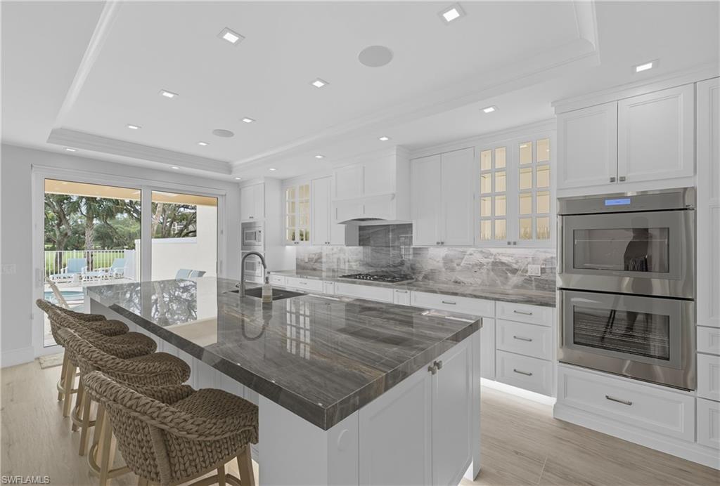 Kitchen with a tray ceiling, appliances with stainless steel finishes, tasteful backsplash, white cabinetry, and recessed lighting