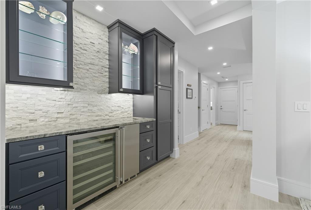 Bar area featuring beverage cooler, light stone counters, light wood finished floors, glass insert cabinets, and recessed lighting