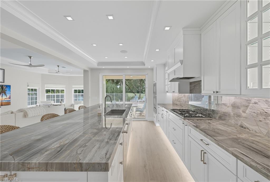 Kitchen featuring white cabinets, a tray ceiling, tasteful backsplash, a large island, and light wood-type flooring