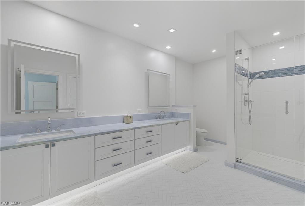 Bathroom featuring a shower stall, double vanity, and recessed lighting
