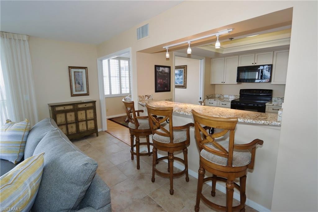 Kitchen with light stone countertops, a kitchen breakfast bar, rail lighting, black appliances, and light tile floors