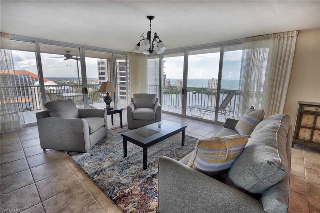 Tiled living room featuring a wall of windows, a water view, and ceiling fan with notable chandelier