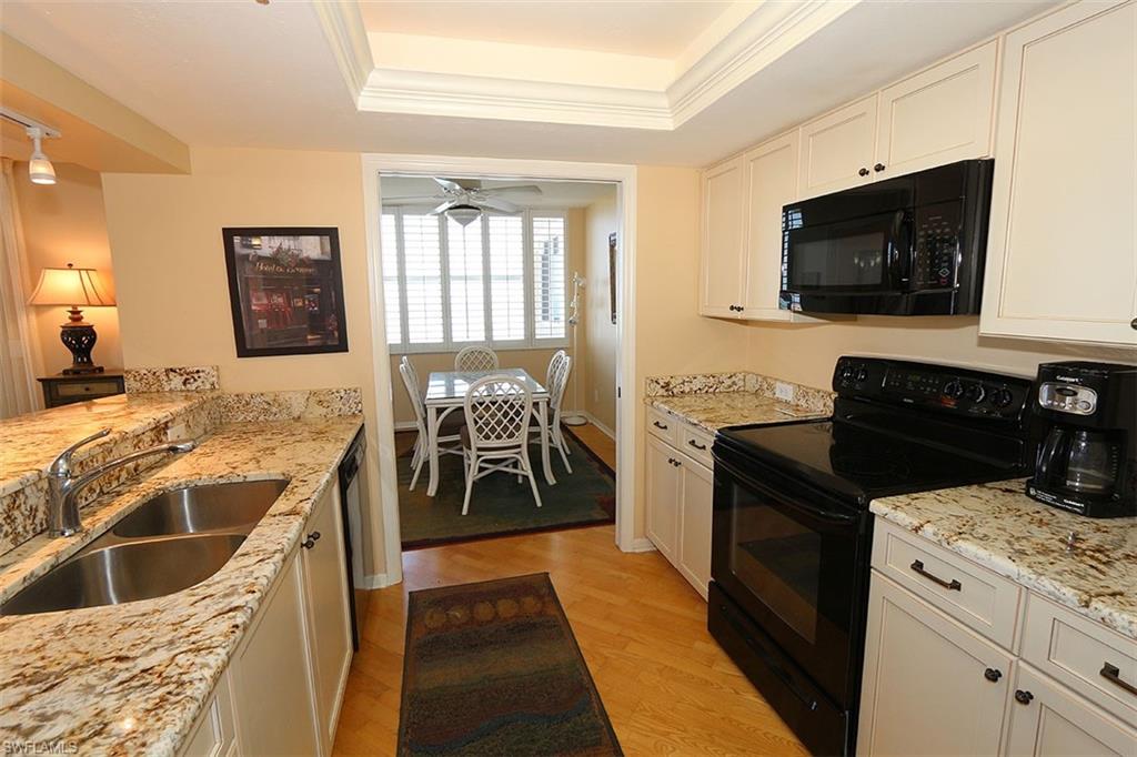 Kitchen with light hardwood / wood-style flooring, a raised ceiling, white cabinetry, black appliances, and sink