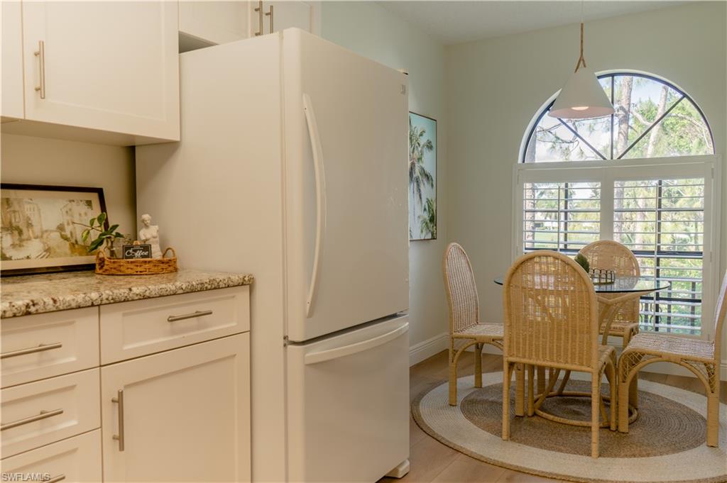 Kitchen featuring light wood-type flooring, light stone counters, freestanding refrigerator, and white cabinetry