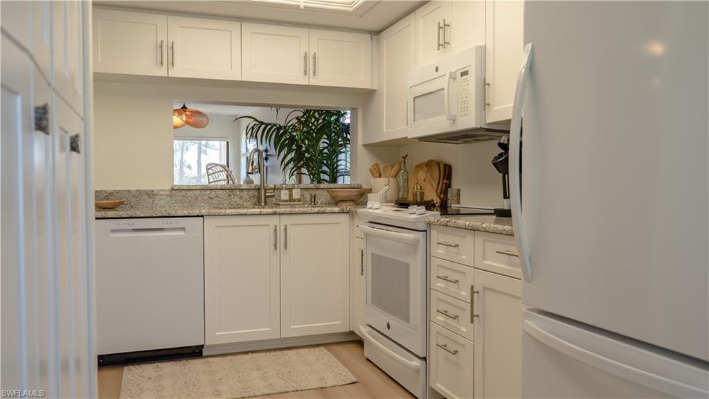 Kitchen with white cabinets, a sink, white appliances, light wood-style floors, and light stone countertops
