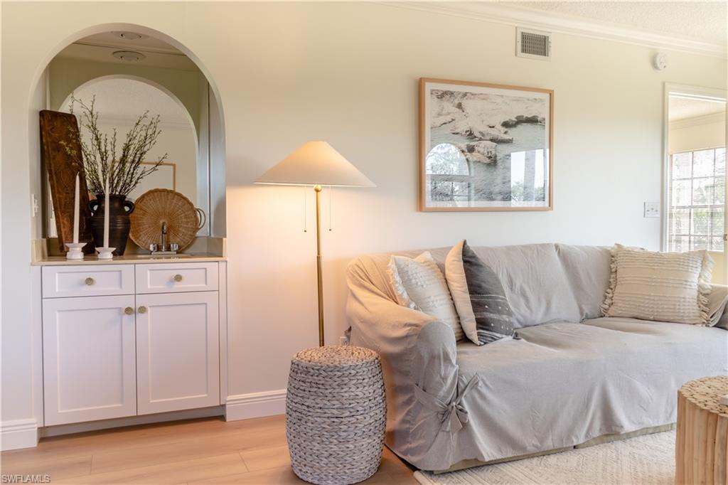 Living area with light wood-style floors, crown molding, visible vents, and arched walkways