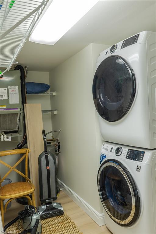 Clothes washing area featuring stacked washer and dryer, laundry area, baseboards, and wood finished floors