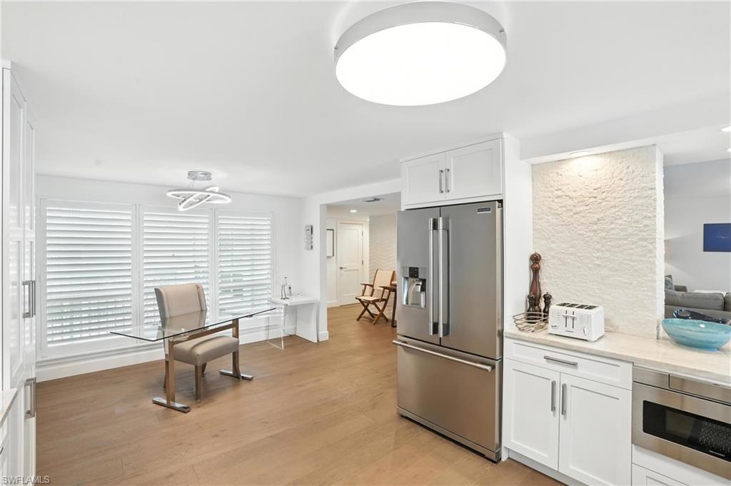 Kitchen with stainless steel appliances, white cabinetry, light wood-style flooring, and light stone counters