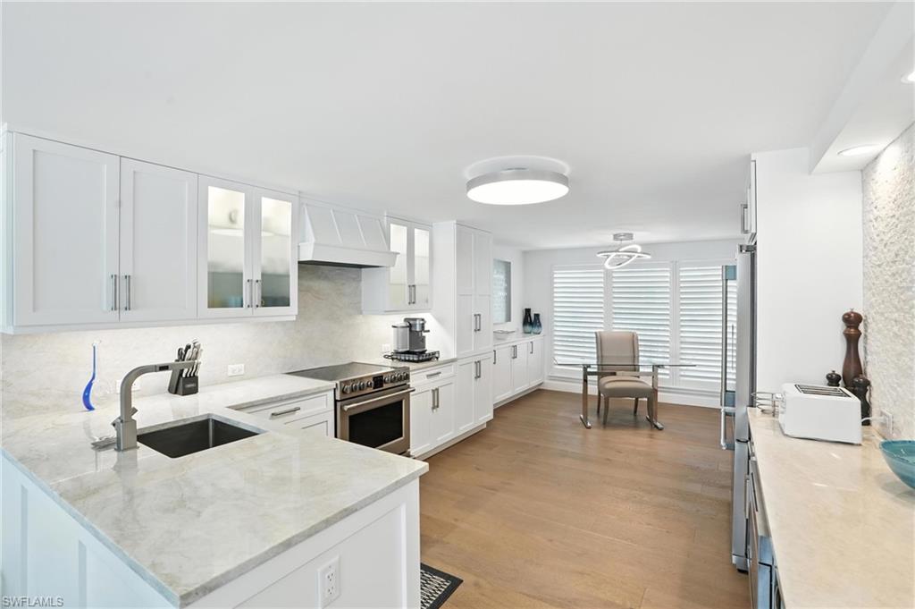 Kitchen featuring high end stainless steel range oven, custom exhaust hood, white cabinetry, light wood-type flooring, and tasteful backsplash