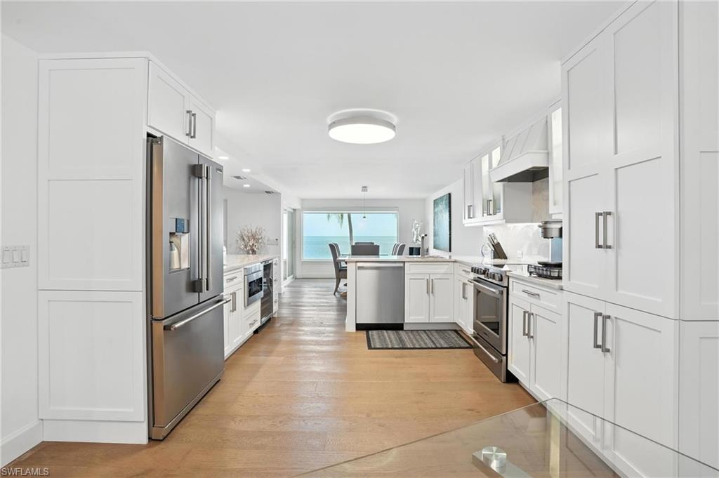 Kitchen featuring appliances with stainless steel finishes, a peninsula, white cabinetry, light countertops, and light wood-style floors