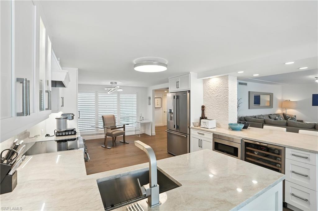 Kitchen featuring appliances with stainless steel finishes, wine cooler, white cabinets, light stone counters, and wood finished floors