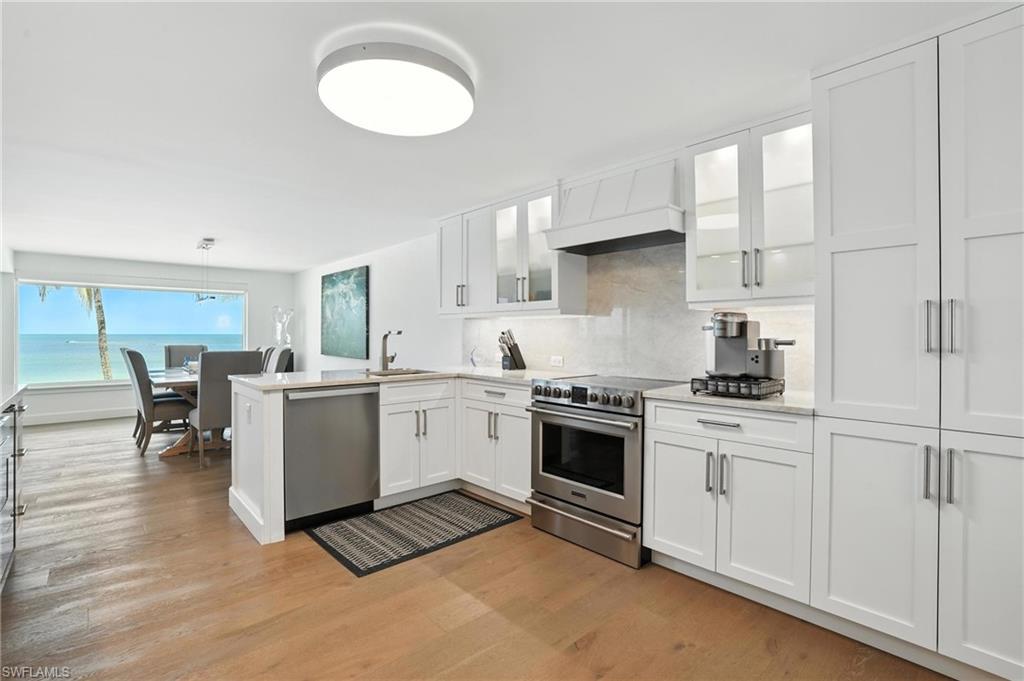Kitchen with appliances with stainless steel finishes, a peninsula, light wood finished floors, custom exhaust hood, and white cabinets