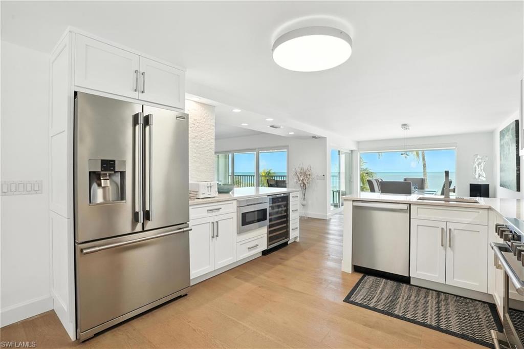 Kitchen featuring stainless steel appliances, wine cooler, light wood-style flooring, white cabinetry, and recessed lighting