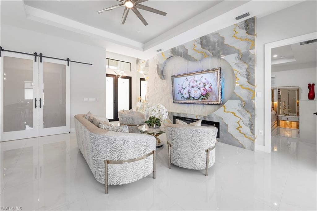 Living space featuring a dramatic accent wall with integrated fireplace, tray ceiling, and polished tile flooring