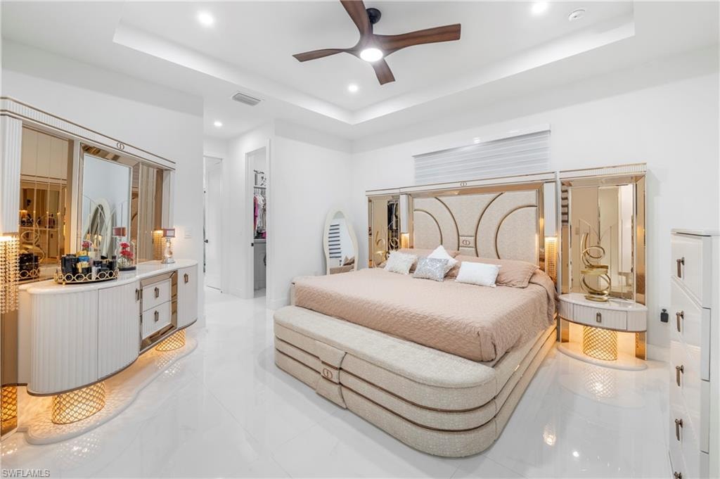 Sleek bedroom featuring a tray ceiling with recessed lighting, a modern ceiling fan, polished white tile flooring, and a large window with horizontal blinds