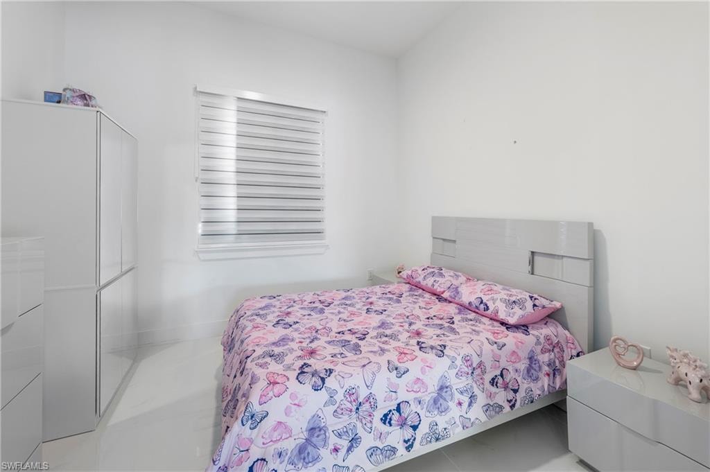 Bright interior room featuring a window with horizontal blinds, white walls, and a light-toned bed frame with a matching nightstand