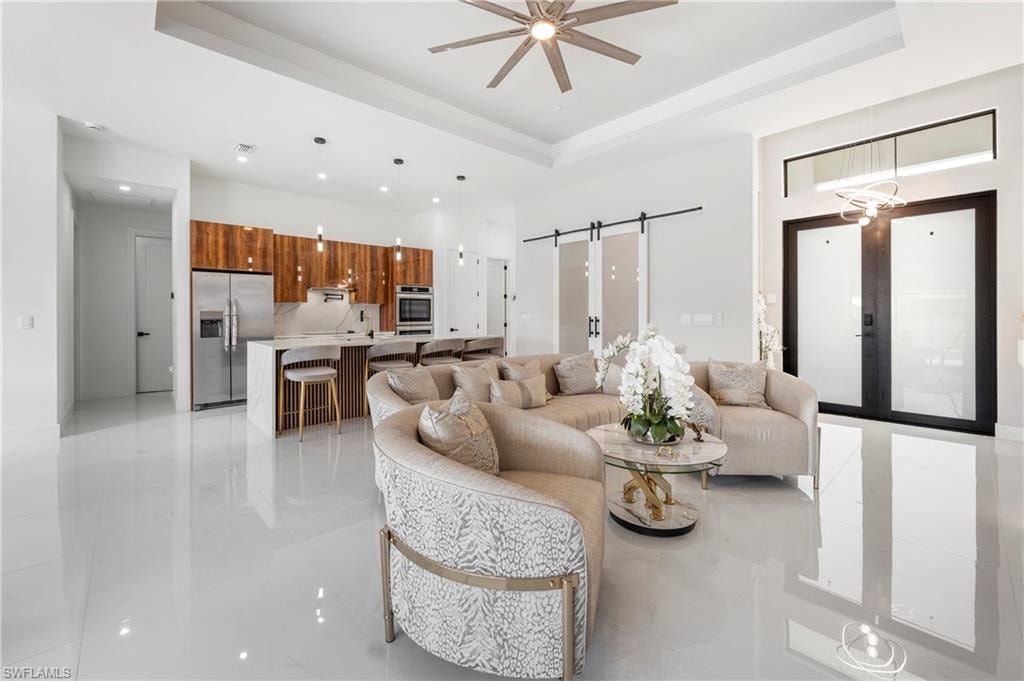 Open-concept living space with sleek white flooring, a kitchen island with seating, stainless steel appliances, and wood-finish cabinetry