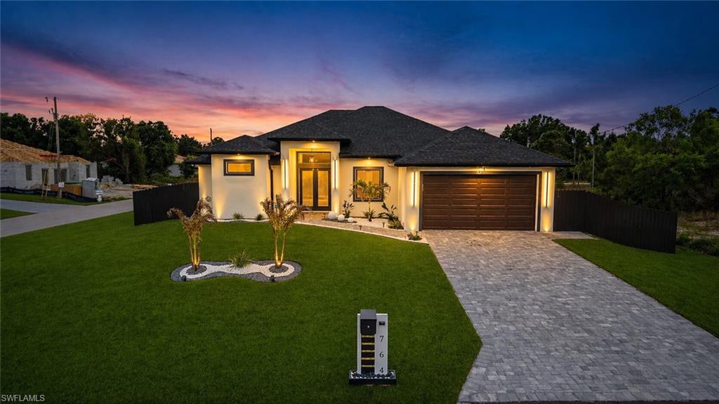 Modern stucco exterior with a dark shingle roof, paver driveway, and a two-car garage